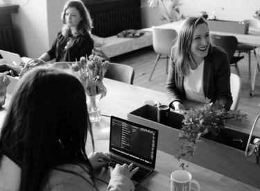 Women sitting at tables facing each other while working on computers